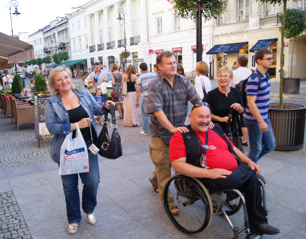 Po ulicy Nowy Świat w warszawie idzie kilka osób, w tym jedna na wózku inwalidzkim